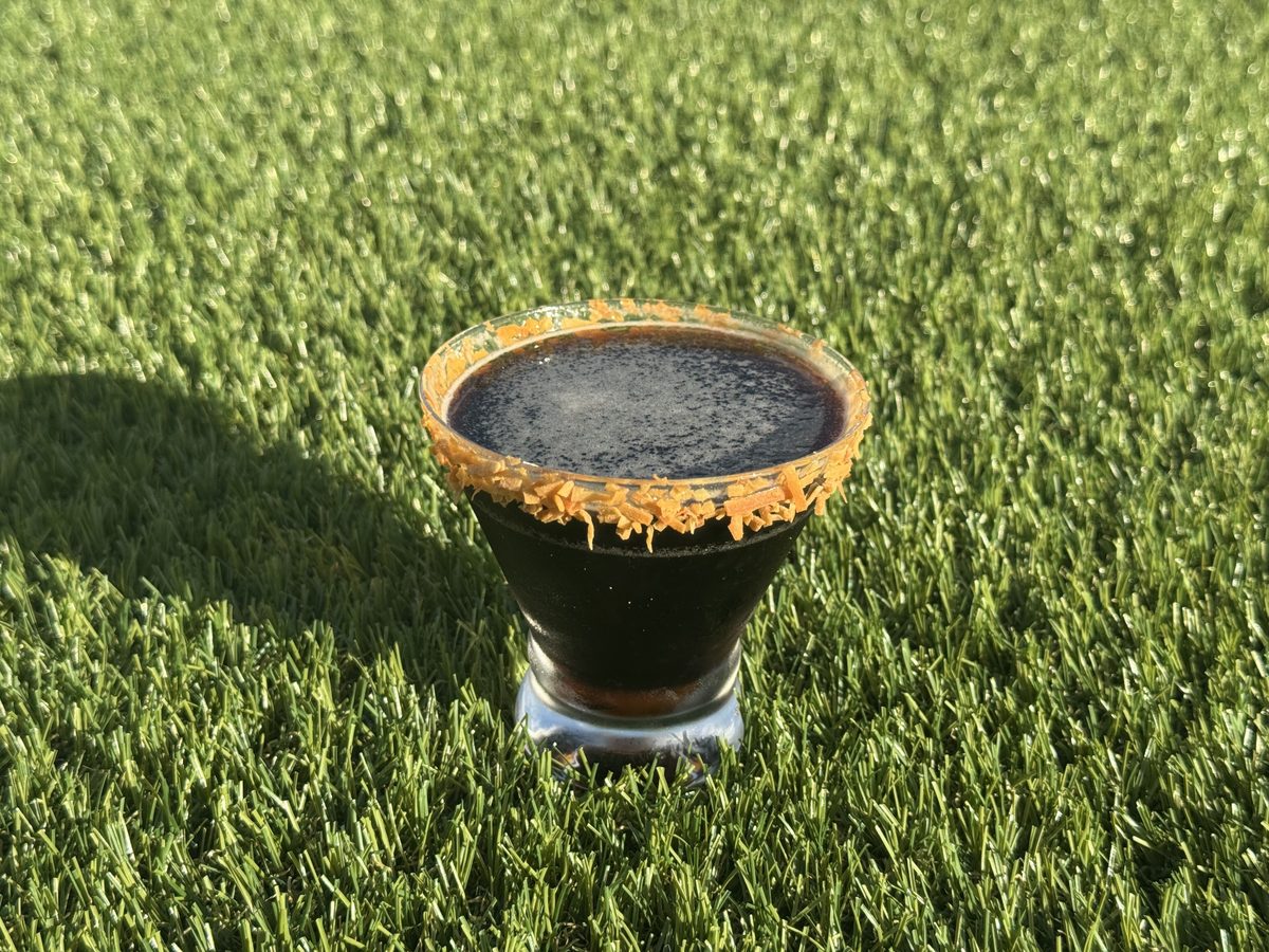 A dark espresso-style cocktail with a sugared rim, set on turf