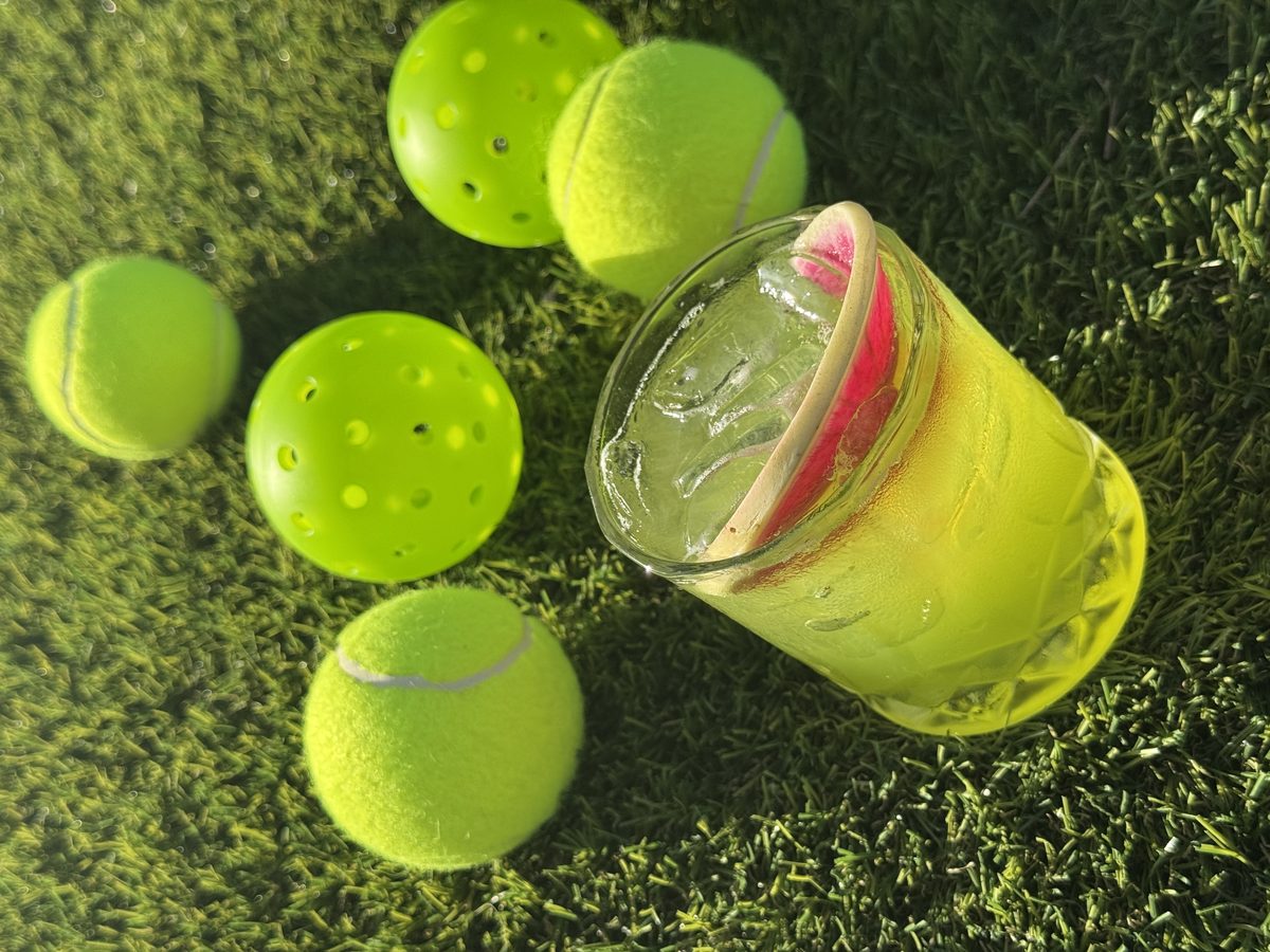 A lime-green cocktail resting on turf beside tennis and pickleball balls