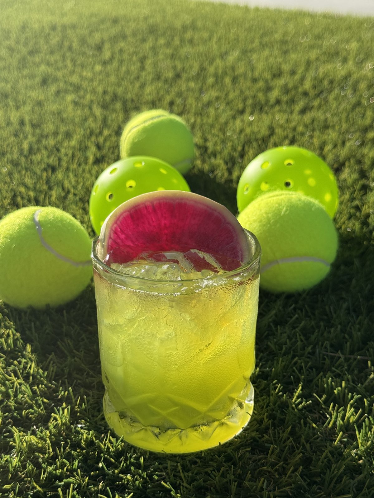 A bright lime cocktail beside tennis balls