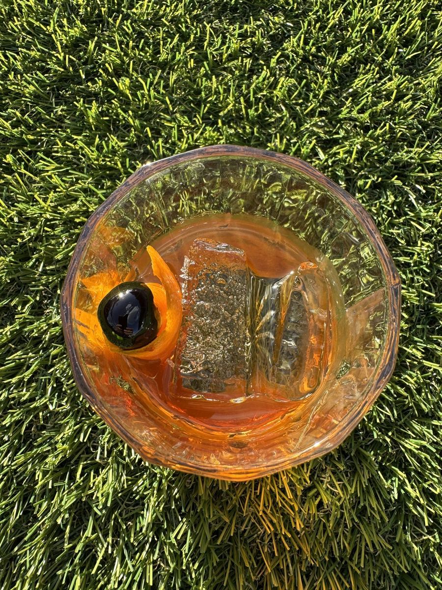 An orange-hued old fashioned with a large ice cube