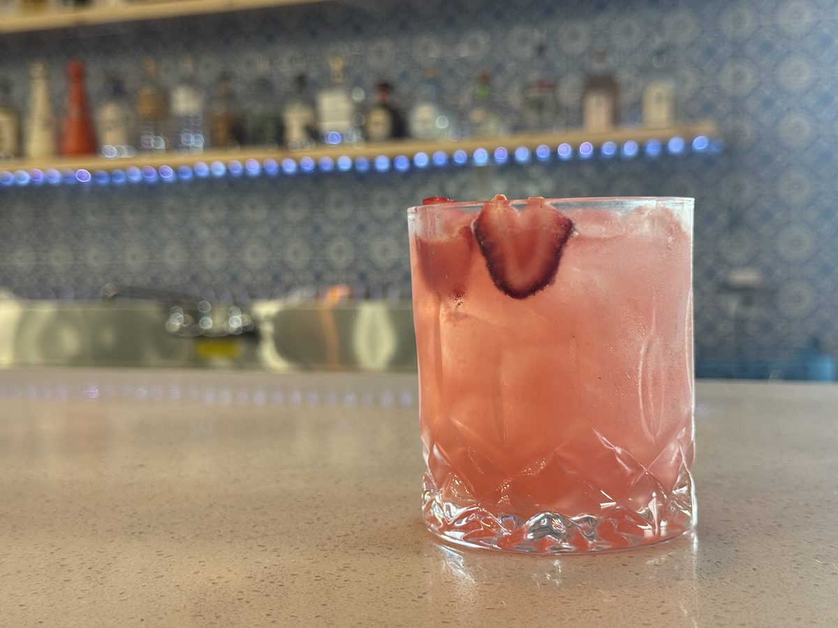 A pink cocktail garnished with strawberry on the Courtside Cantina bar