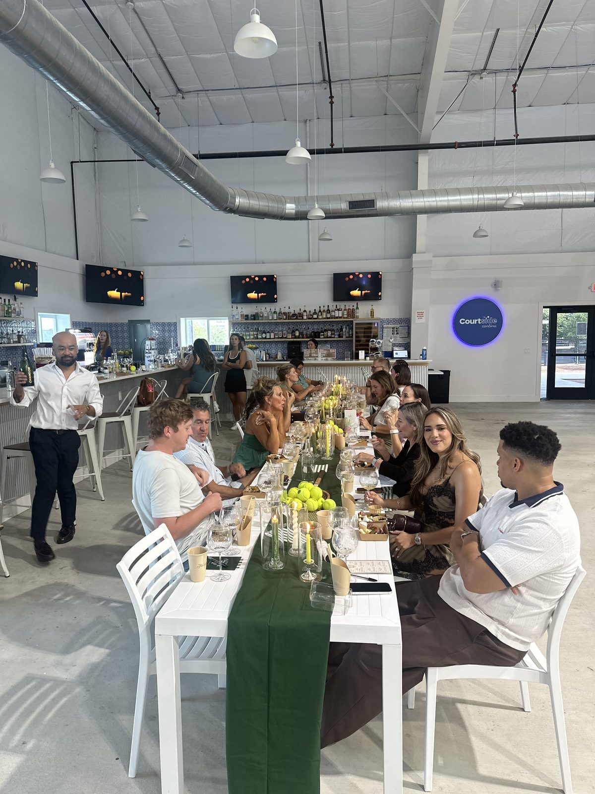 A long table of guests eating and drinking together in the Courtside Cantina dining area