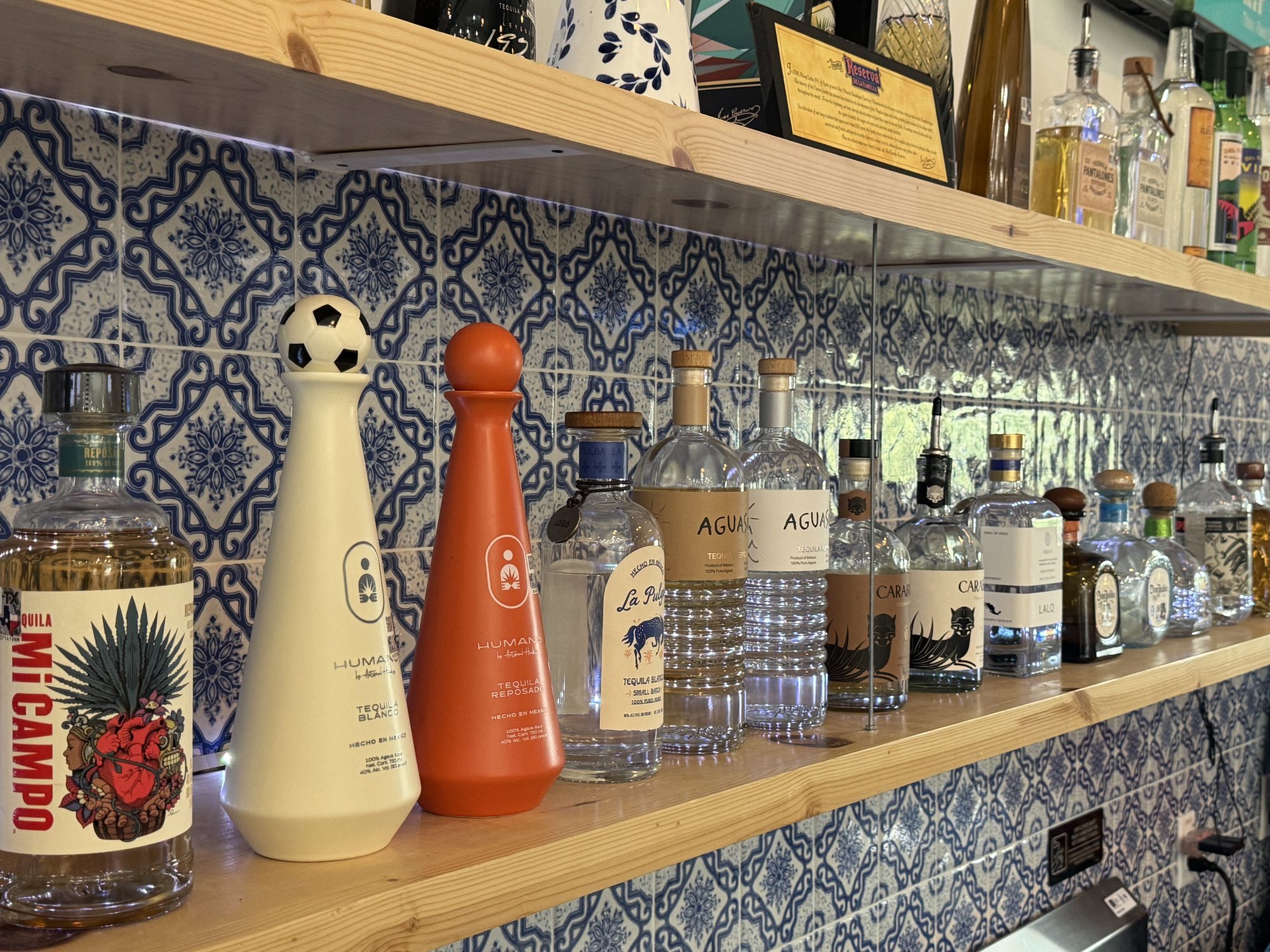 The bar at Courtside Cantina in Buda, Texas, backed by blue tile and shelves of tequila and whiskey