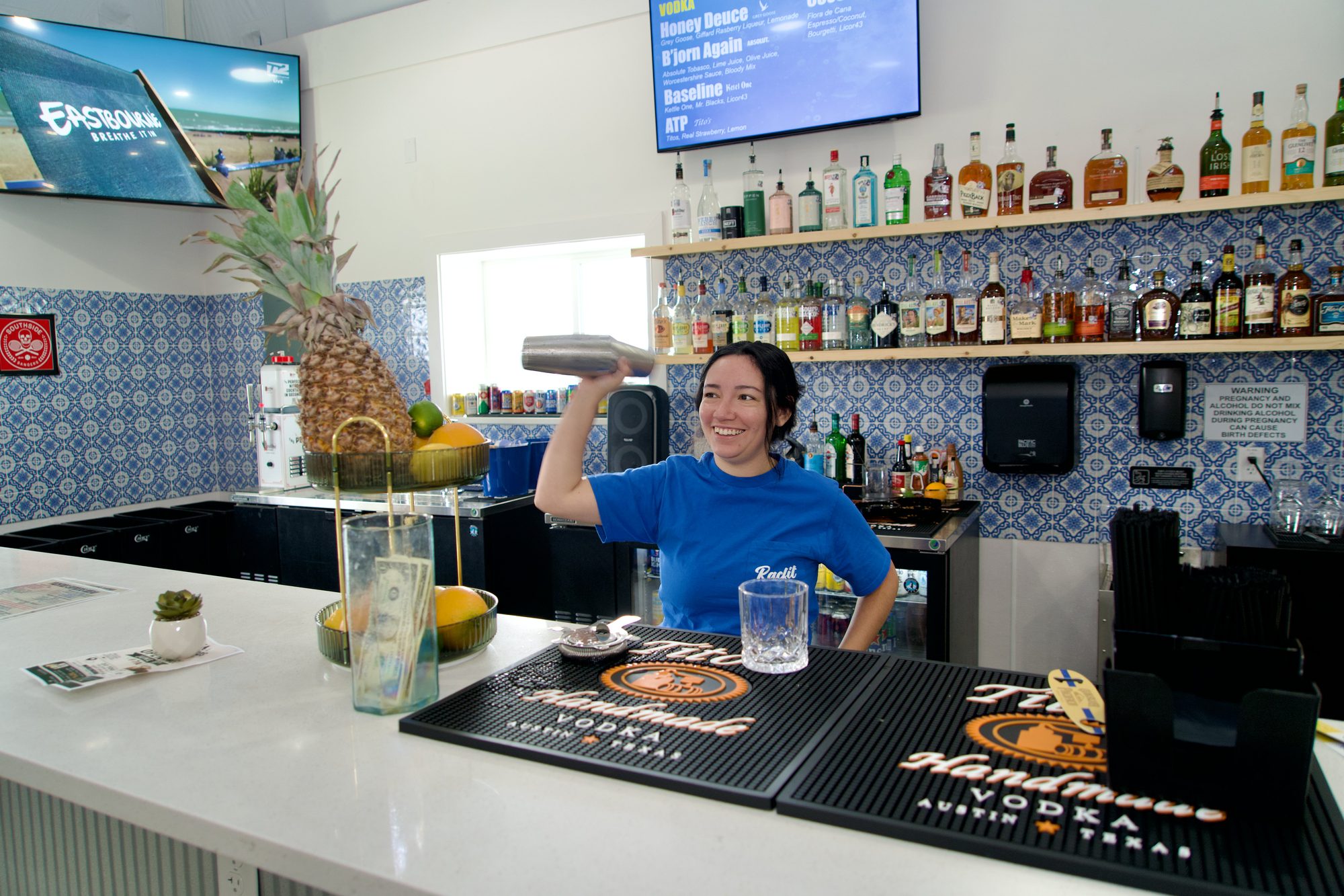 A bartender working behind the Courtside Cantina bar with TVs overhead