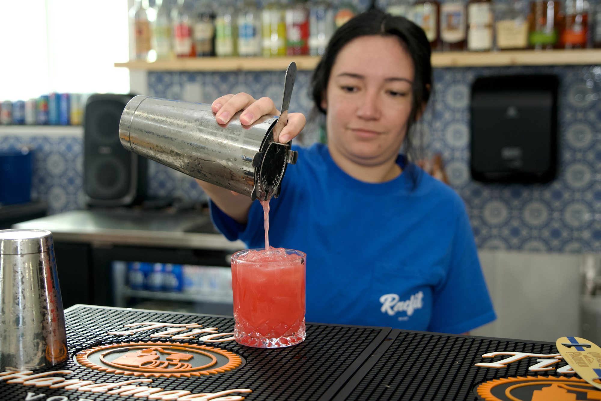 A bartender straining a red cocktail into a glass at Courtside Cantina