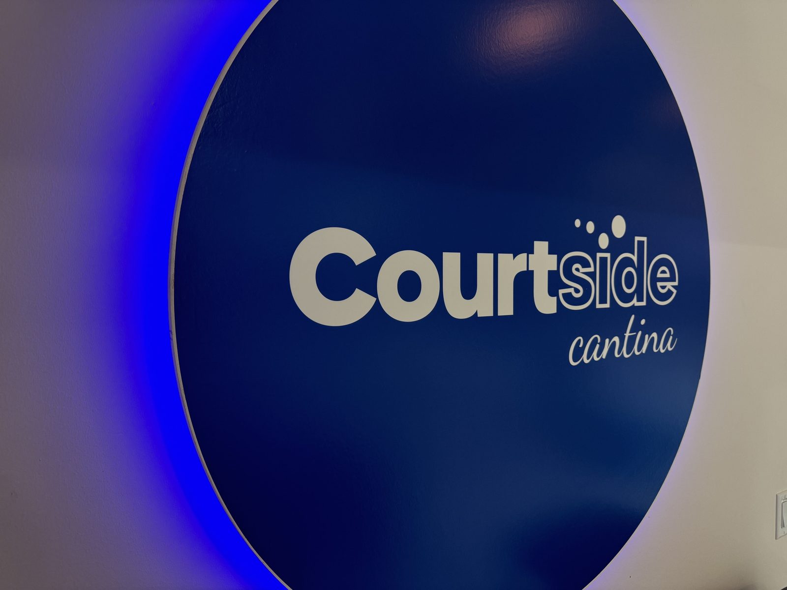 The backlit Courtside Cantina sign glowing blue inside RacFit